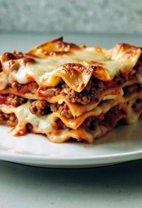 Een stuk opgewarmde lasagne op een wit bordje.