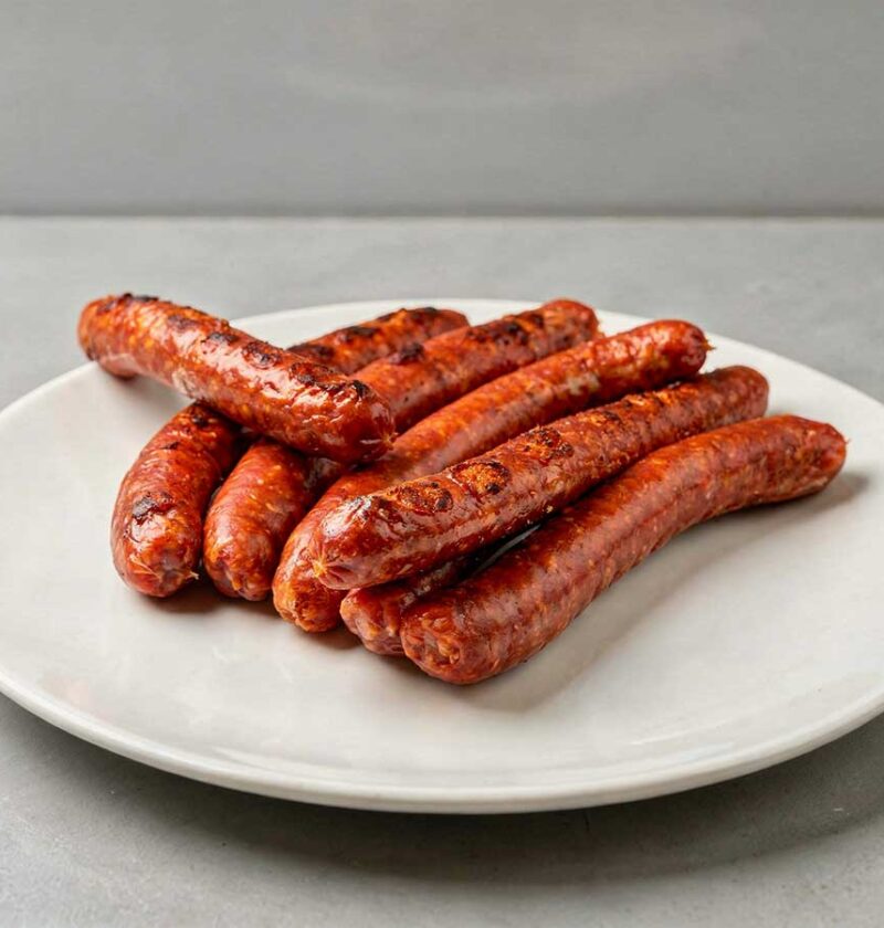 7 gebakken Merguez worstjes op een wit bord.
