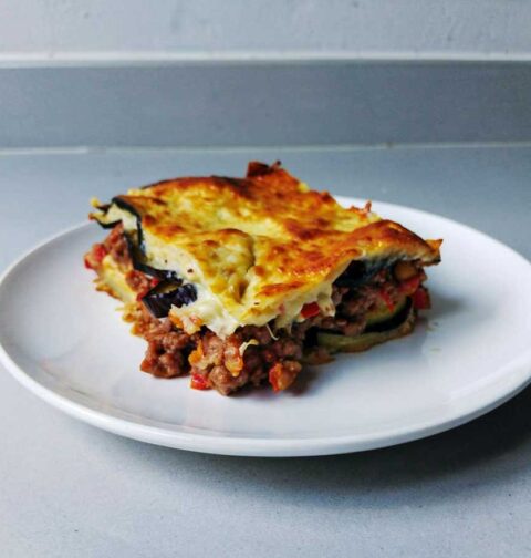 Een opgewarmd stuk moussaka op een wit bord.