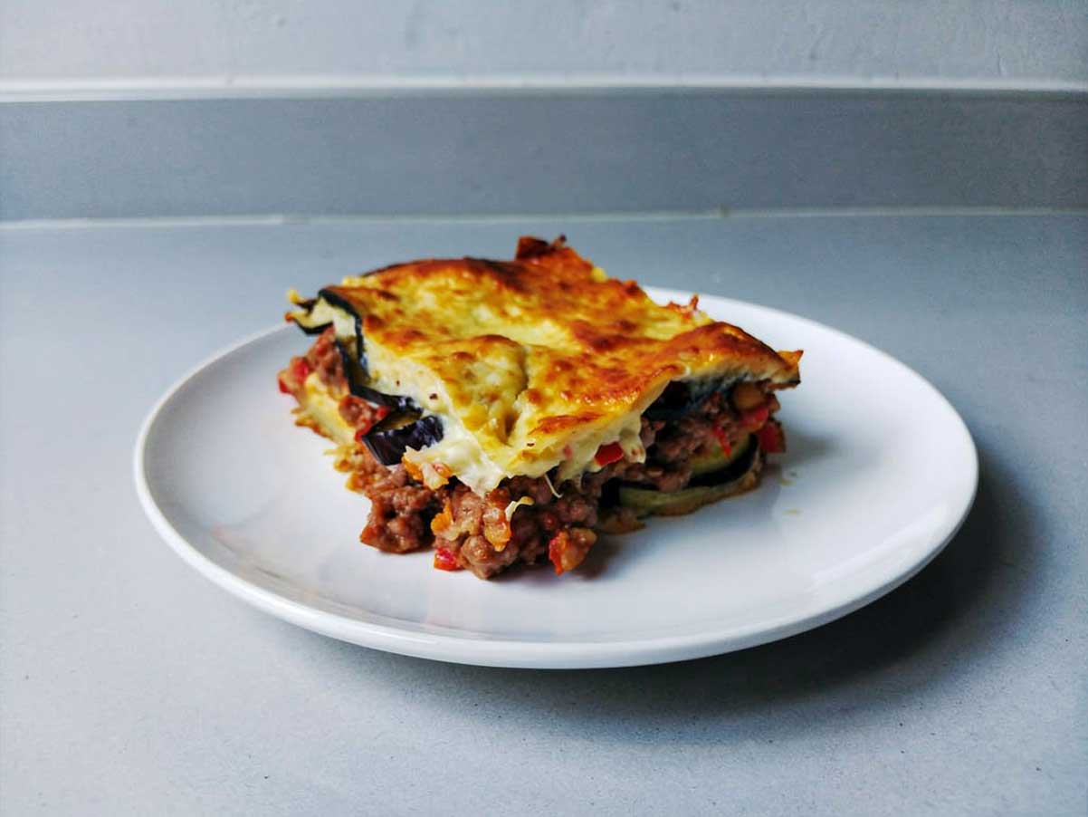 Een opgewarmd stuk moussaka op een wit bord.