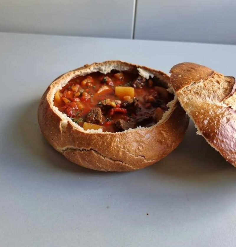 Een uitgehold wit, rond brood, waarin Goulassoep is gedaan.