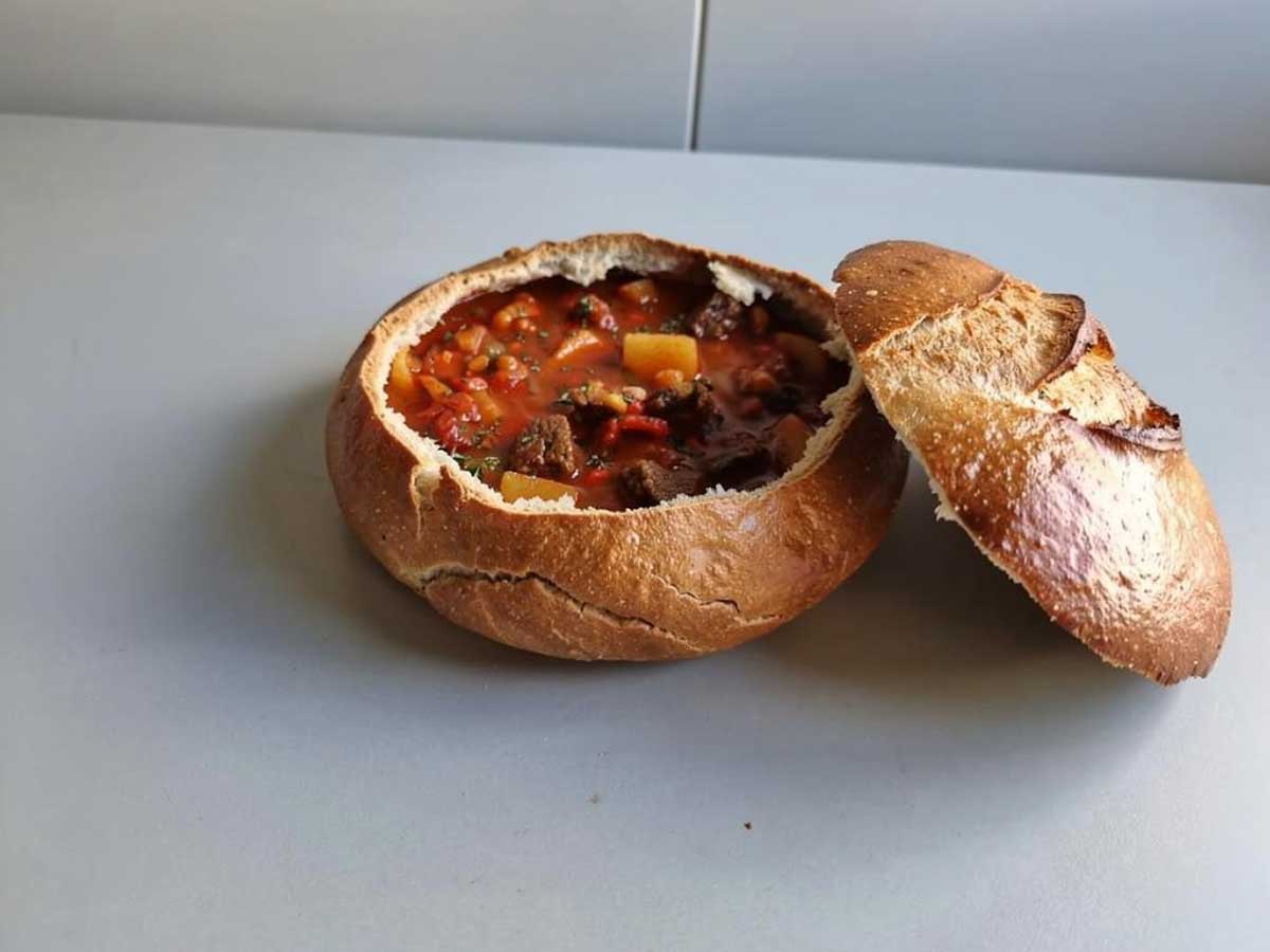 Een uitgehold wit, rond brood, waarin Goulassoep is gedaan.