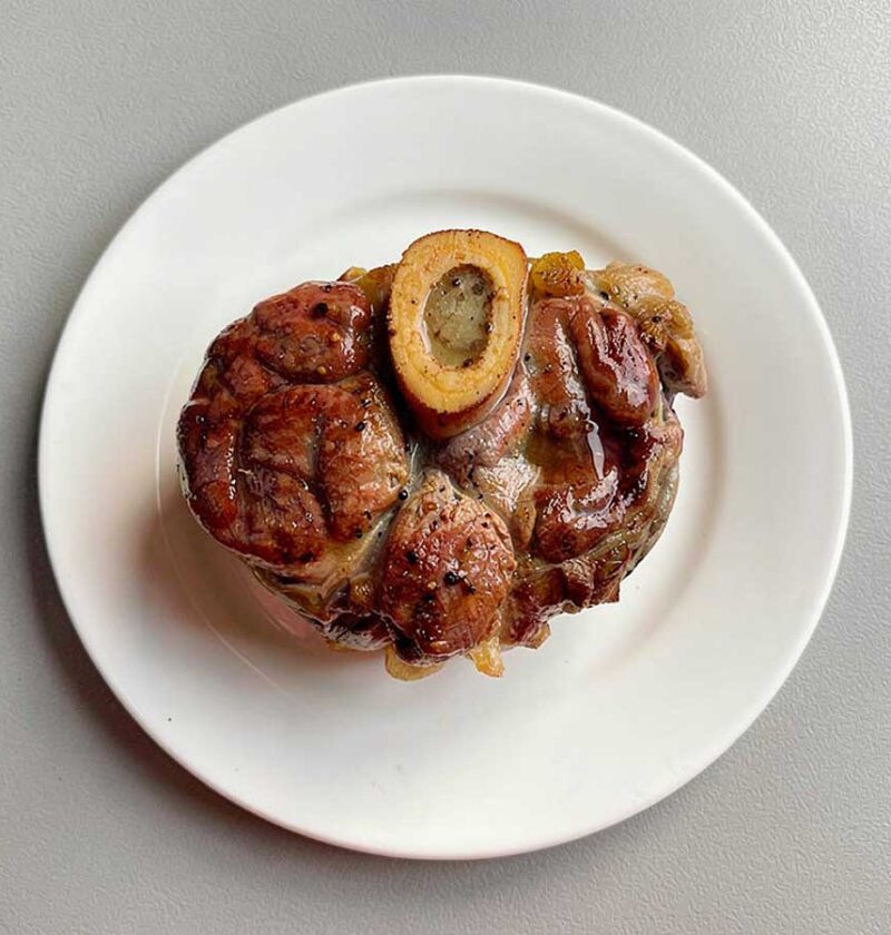 Een opgewarmde ossobuco op een wit bordje.
