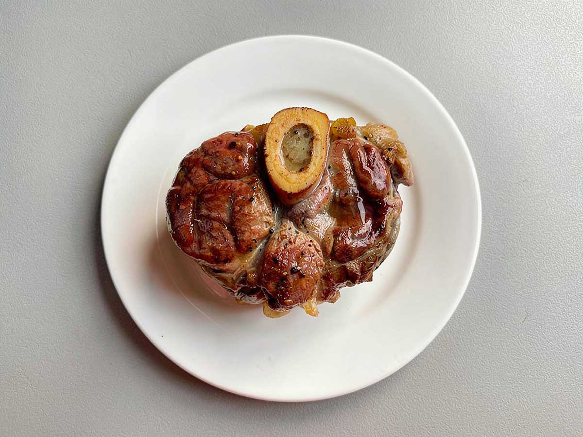 Een opgewarmde ossobuco op een wit bordje.
