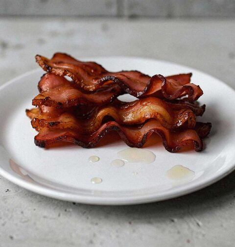 4 gebakken plakken pancetta op een wit bordje.