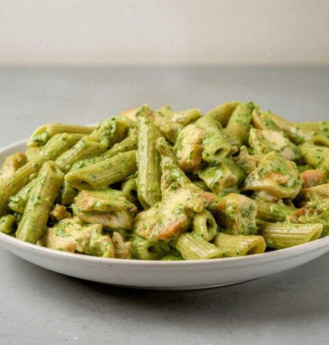 Een bord met pasta pesto met stukjes gebakken kip.