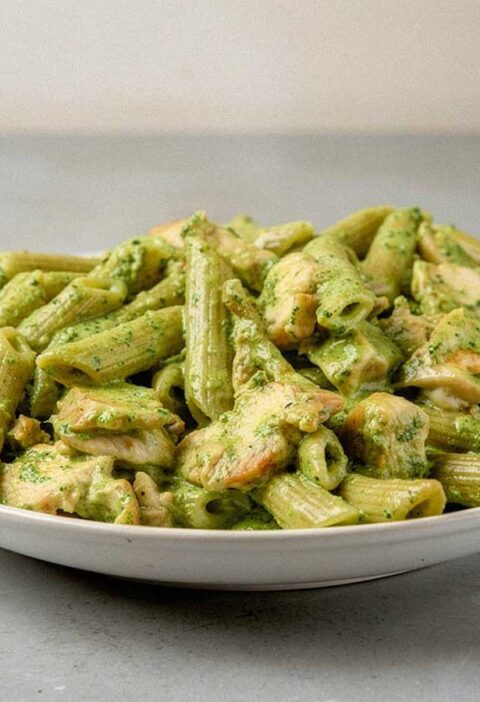 Een bord met pasta pesto met stukjes gebakken kip.
