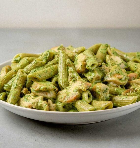Een bord met pasta pesto met stukjes gebakken kip.