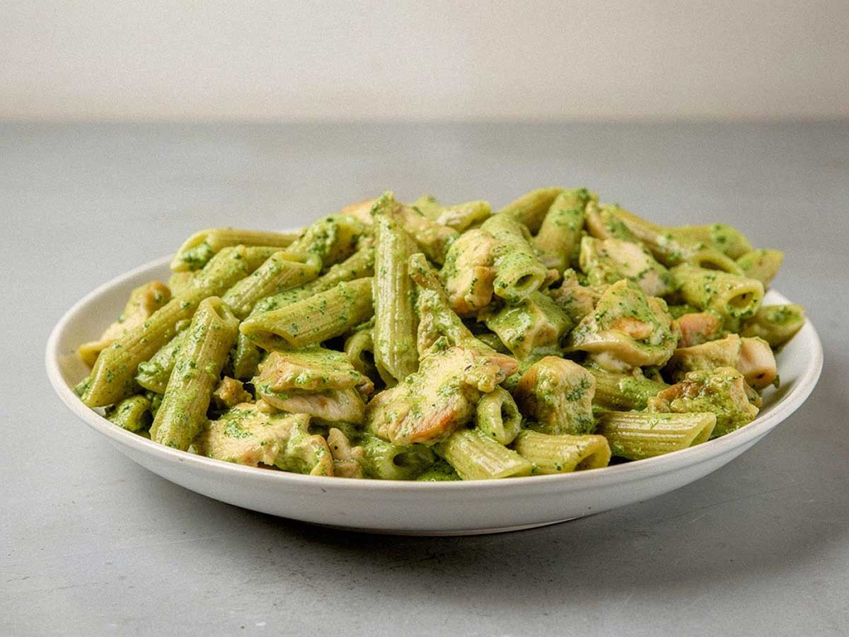 Een bord met pasta pesto met stukjes gebakken kip.
