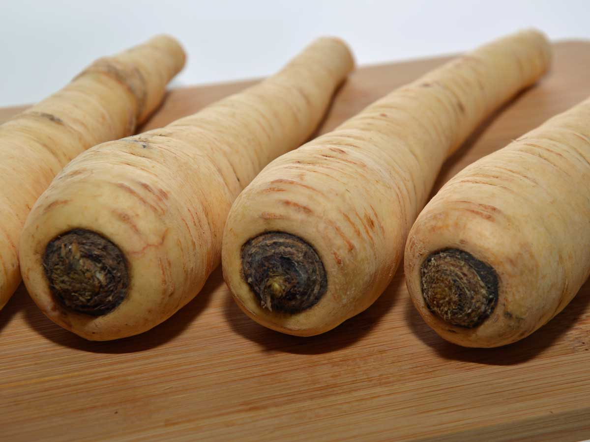 4 pastinaken liggen op een rij op een houten snijplank.