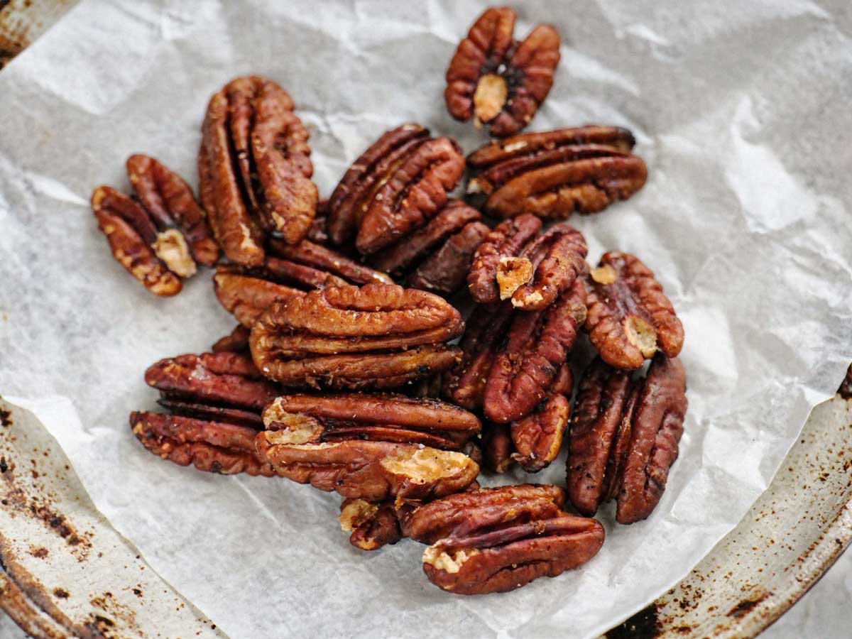 Een handjevol glanzende, goudbruin geroosterde pecannoten op een wit stuk bakpapier.