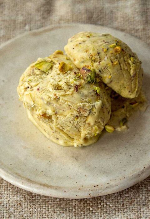 Drie bolletjes groen pistache roomijs op een plat schaaltje met stukjes noot.