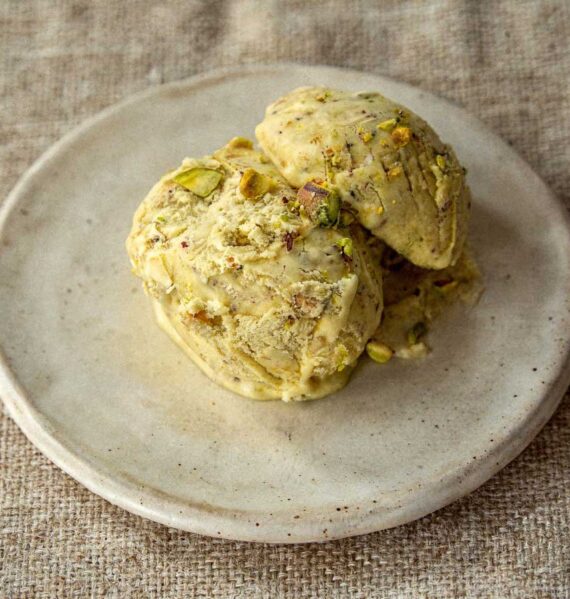 Drie bolletjes groen pistache roomijs op een plat schaaltje met stukjes noot.