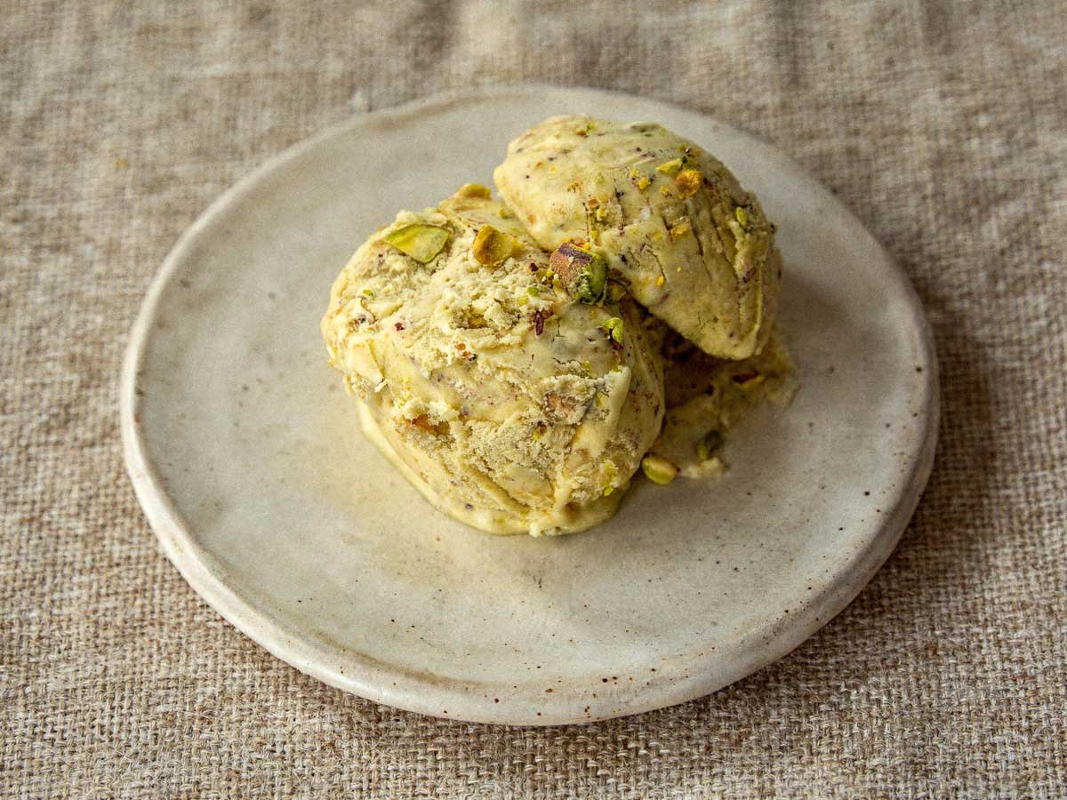 Drie bolletjes groen pistache roomijs op een plat schaaltje met stukjes noot.