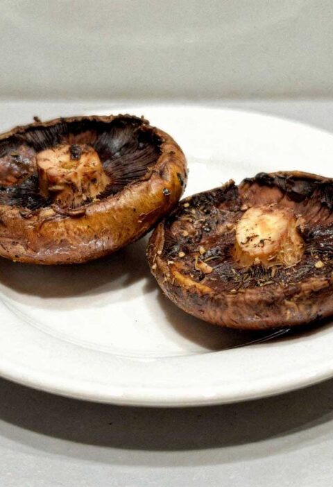 2 gebakken portobello paddenstoelen liggen op een wit bord.