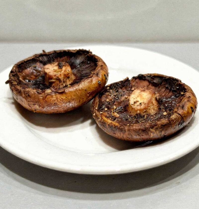 2 gebakken portobello paddenstoelen liggen op een wit bord.