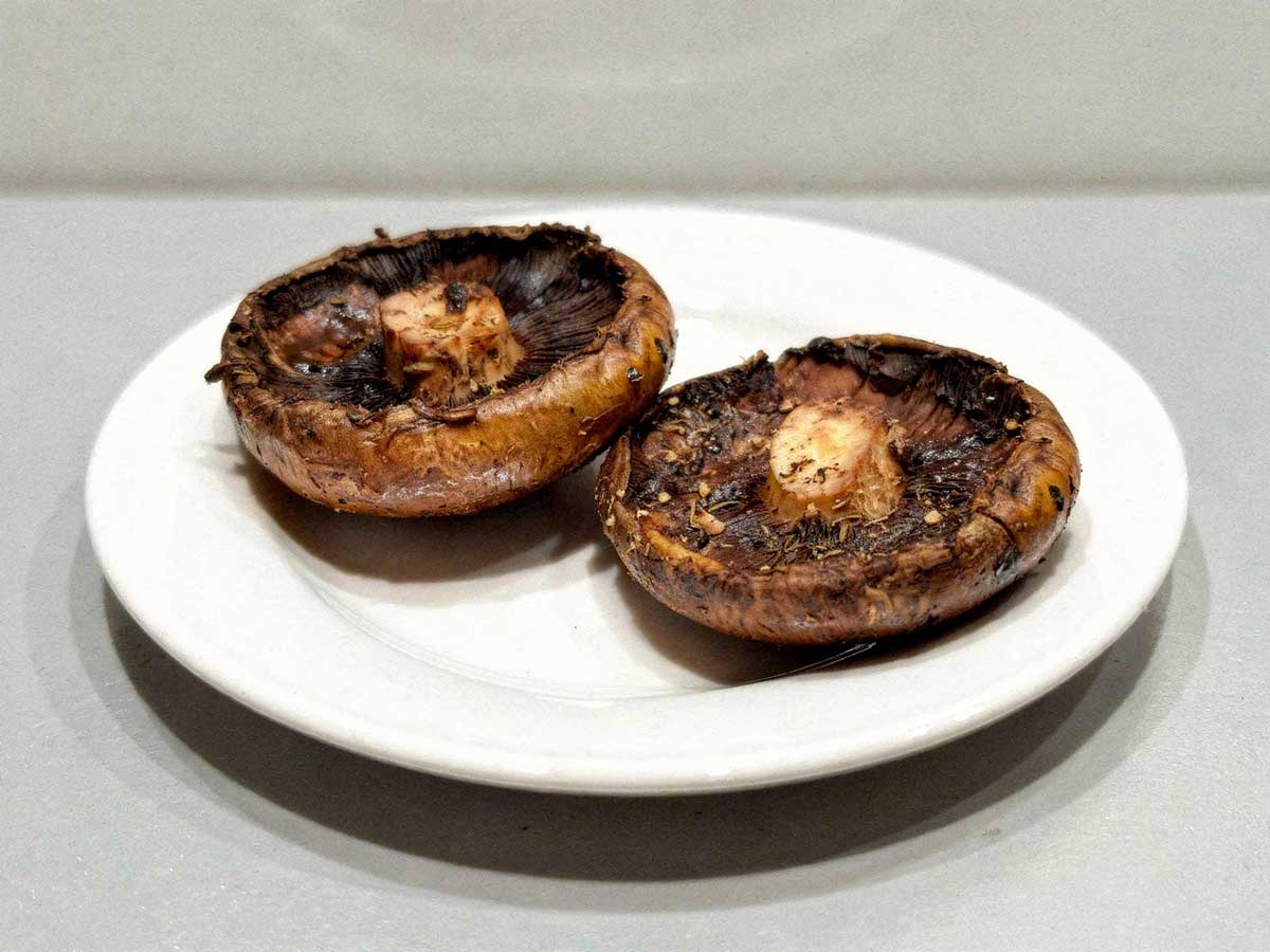 2 gebakken portobello paddenstoelen liggen op een wit bord.
