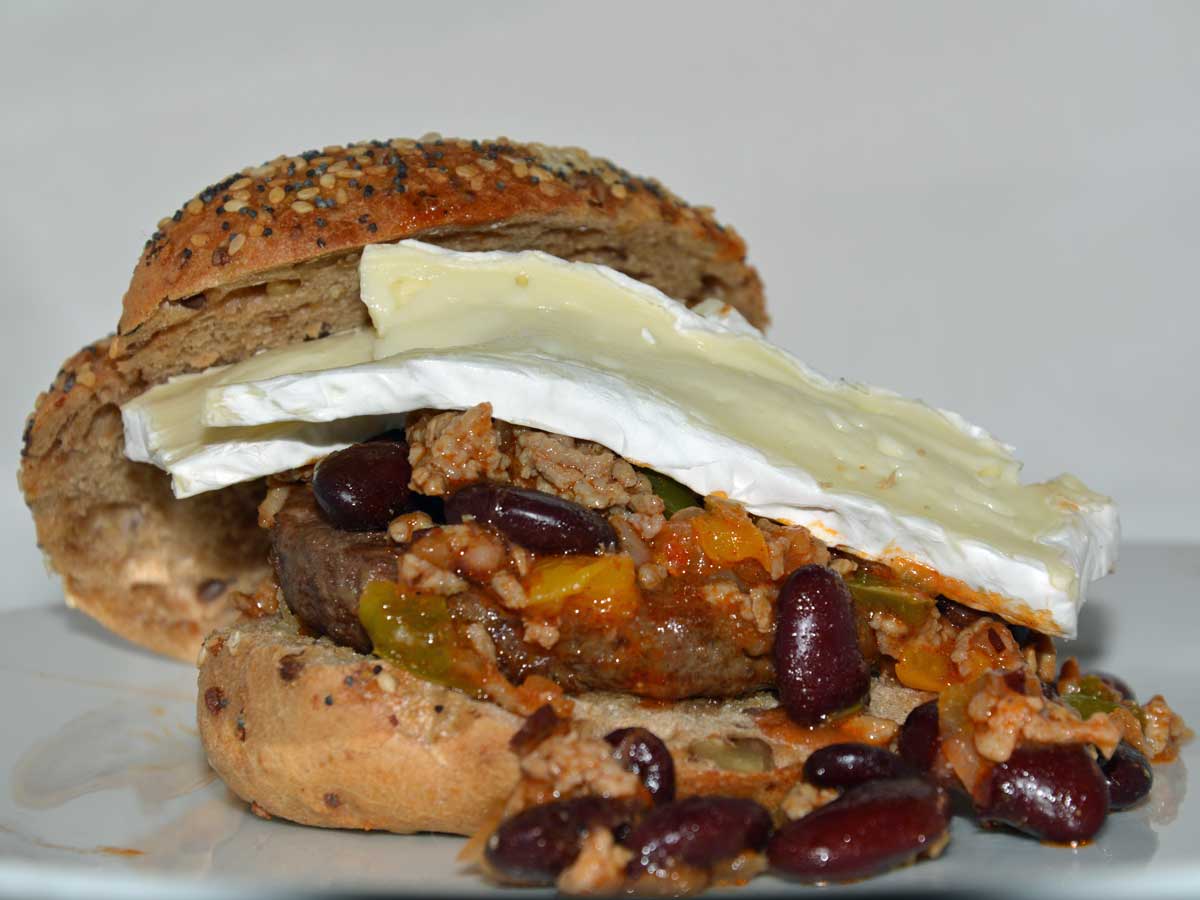 Een zacht broodje met daarop chili con carne en en paar plakken camembert.