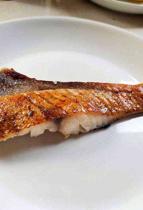 een gebakken red snapperfilet op een wit bordje.
