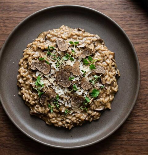 Een donker bord met daarop een overgebleven portie risotto.