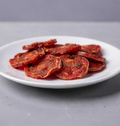 Een wit bordje vol met plakjes gebakken salami.