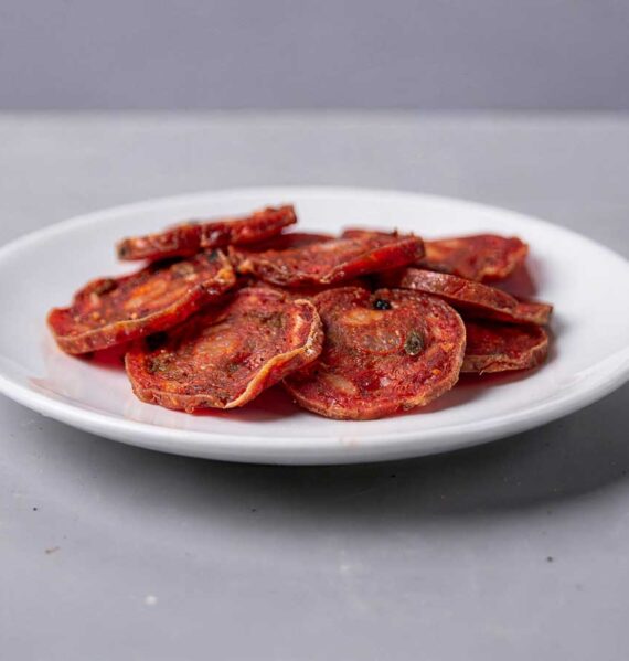 Een wit bordje vol met plakjes gebakken salami.