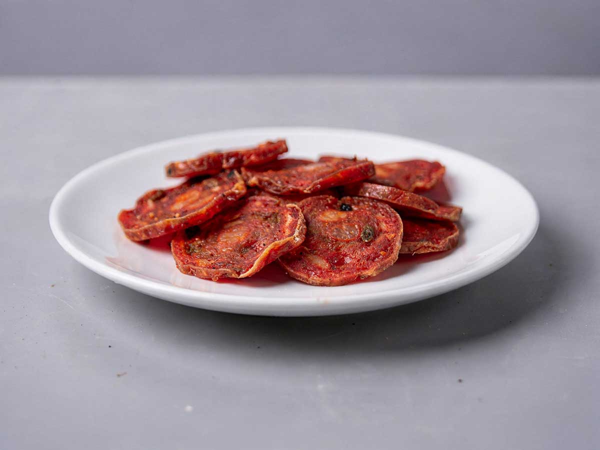 Een wit bordje vol met plakjes gebakken salami.