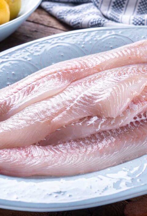 Verse schelvisfilets op een lichtblauw bord, klaar om te bakken.