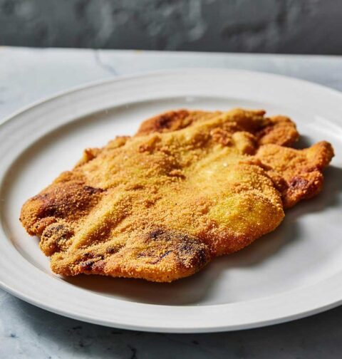 Een grote gebakken schnitzel op een wit bord.