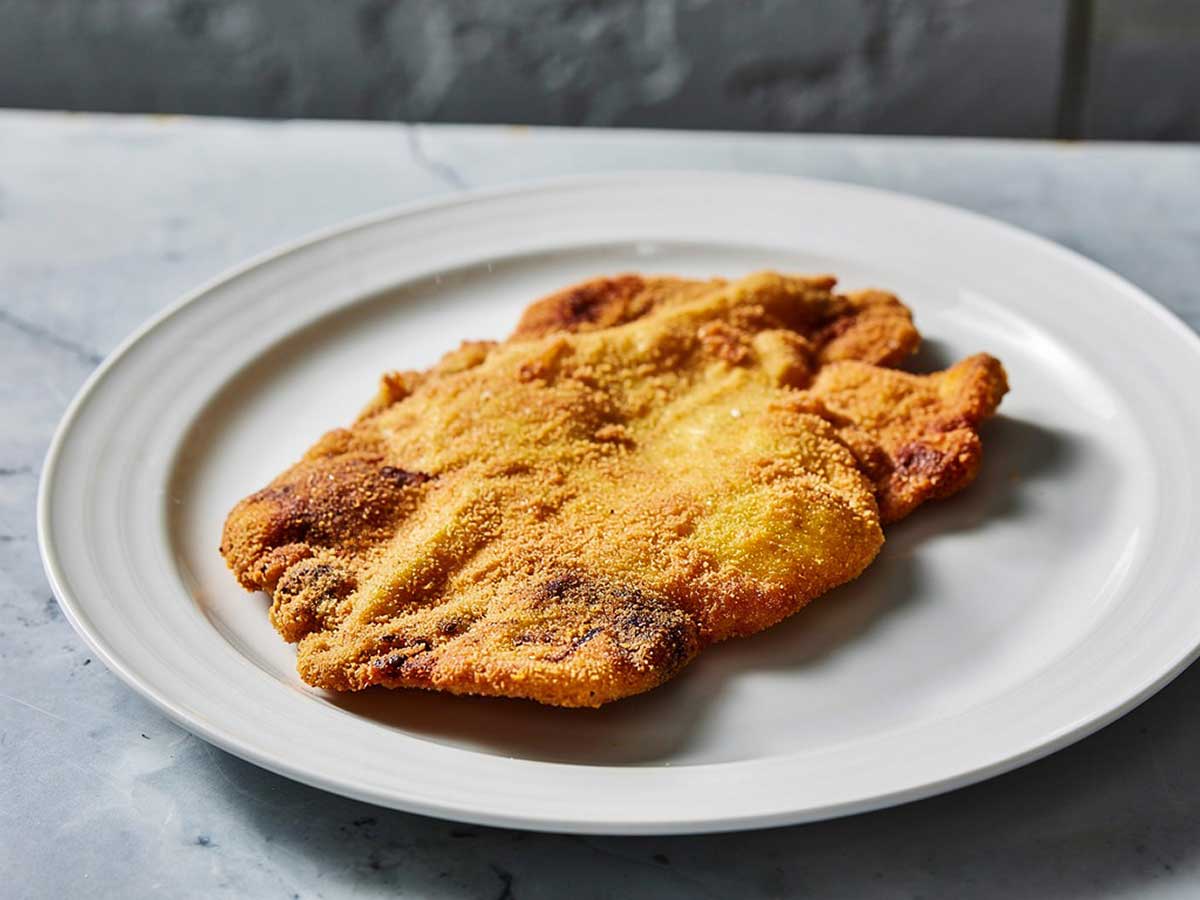 Een grote gebakken schnitzel op een wit bord.