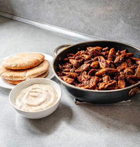 Een koekenpan vol gebakken shoarma, met pitabroodjes en knoflooksaus.