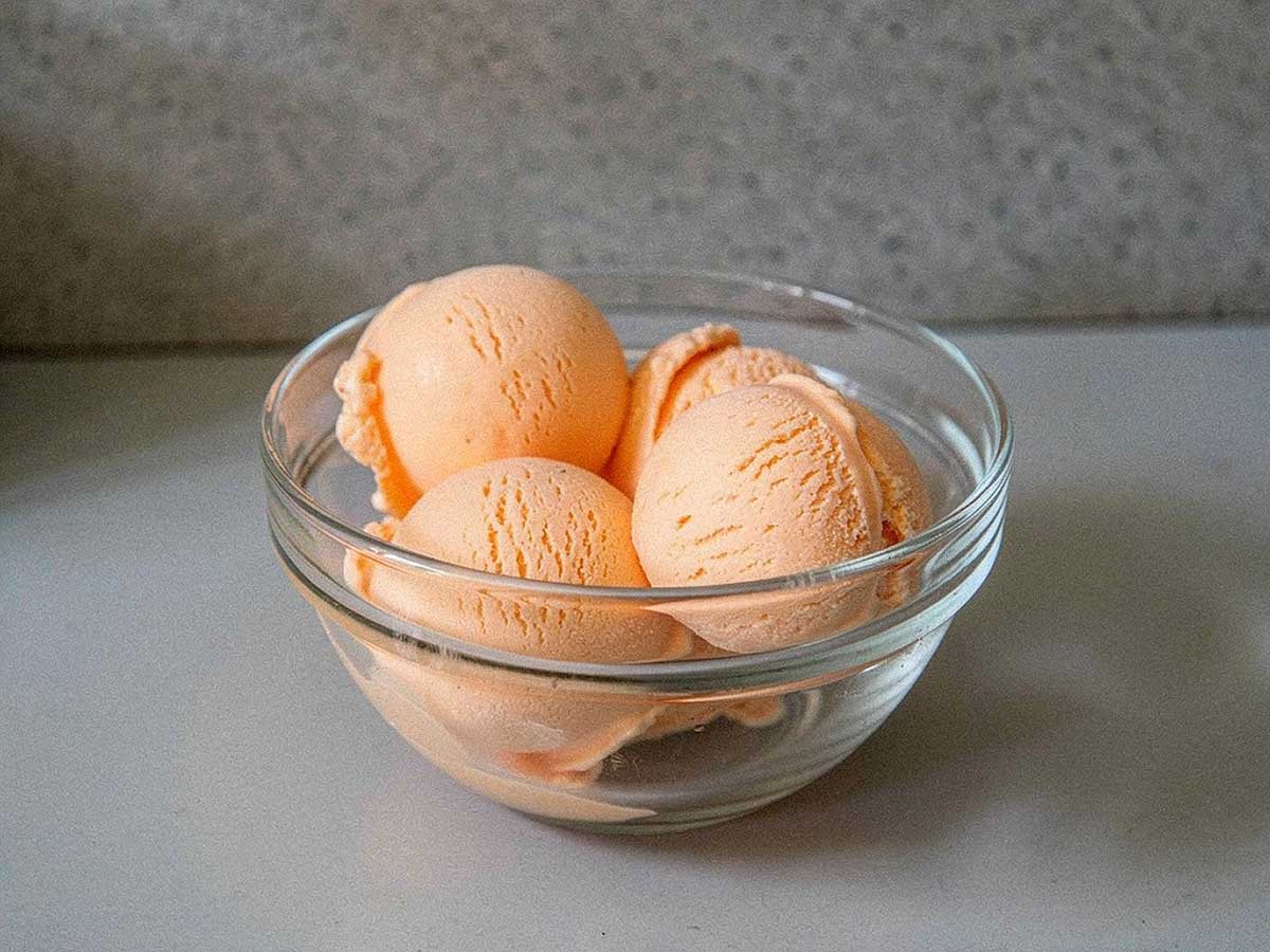 4 bollen sinaasappel roomijs in een glazen schaaltje.