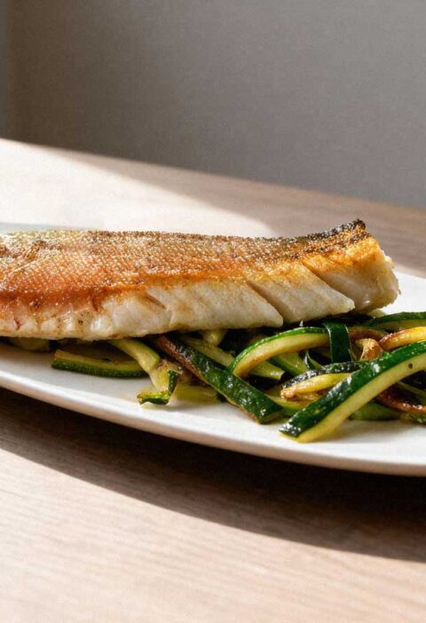 Gebakken snoekfilet op een bedje van groenten, op een witte schaal.