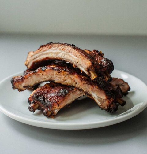 4 gebakken spareribs (stukken) op een wit bordje.