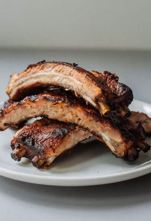 4 gebakken spareribs (stukken) op een wit bordje.
