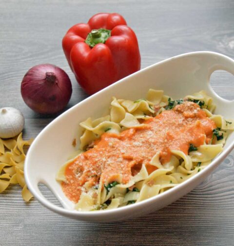 Tagliatelle met paprikasaus in een schaaltje met ernaast verse paprika en ui.