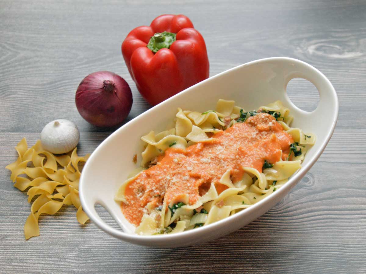 Tagliatelle met paprikasaus in een schaaltje met ernaast verse paprika en ui.