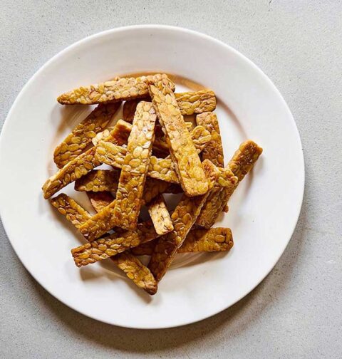 Een wit bord met daarop dunne plakjes gebakken tempeh.