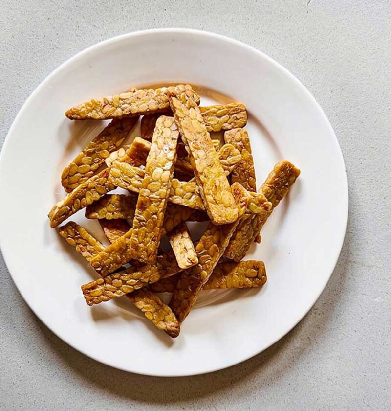 Een wit bord met daarop dunne plakjes gebakken tempeh.