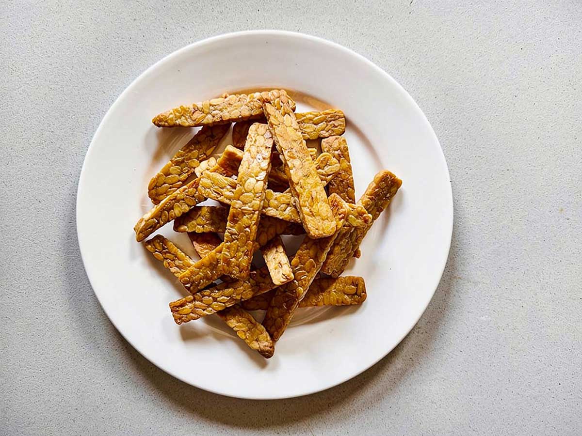 Een wit bord met daarop dunne plakjes gebakken tempeh.