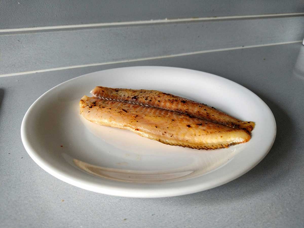 Een gebakken tilapiafilet op een wit bordje.