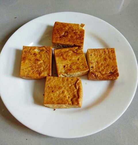 5 blokjes gebakken tofu op een wit bord.