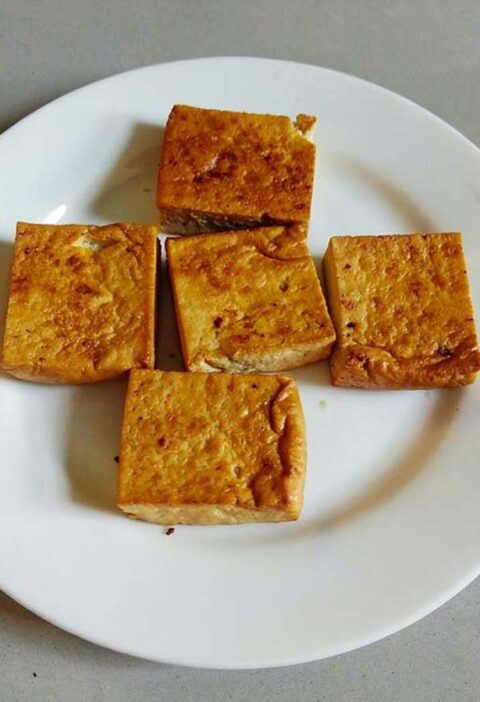 5 blokjes gebakken tofu op een wit bord.