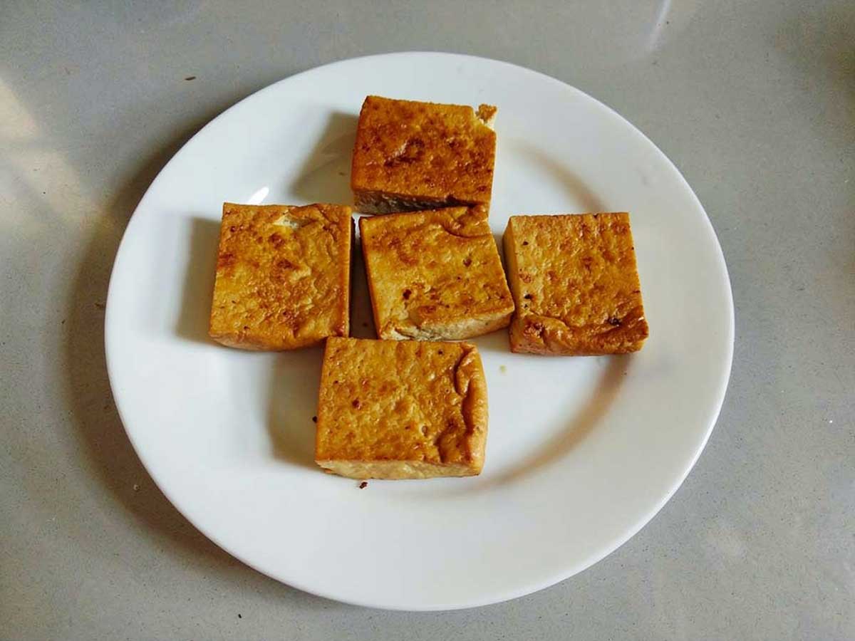 5 blokjes gebakken tofu op een wit bord.