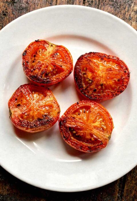 Een wit bord vol met gebakken halve tomaten met de gekaramelliseerde kant boven.