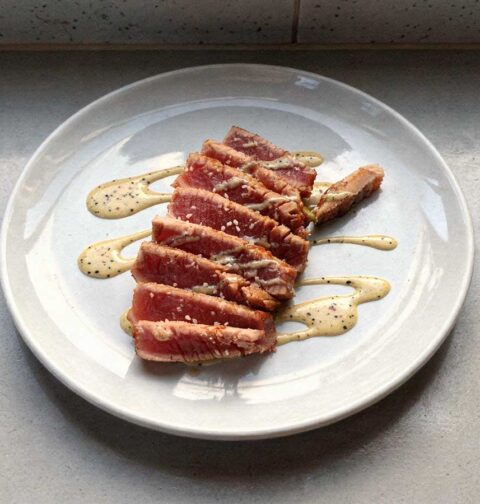 Een aan plakken gesneden tonijnsteak op een wit bord.