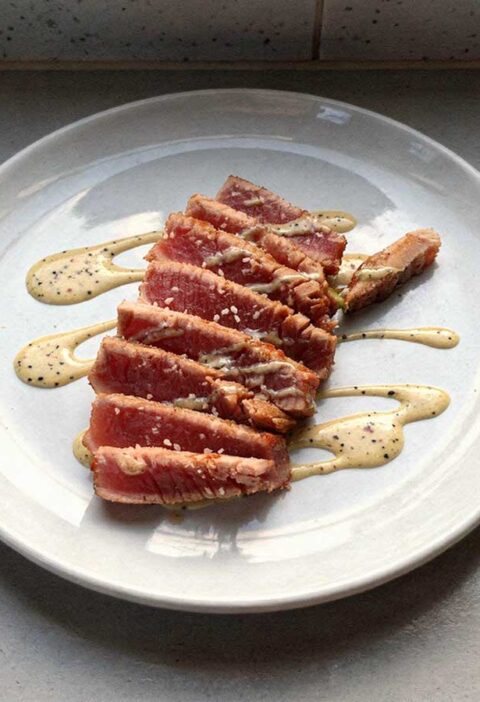 Een aan plakken gesneden tonijnsteak op een wit bord.
