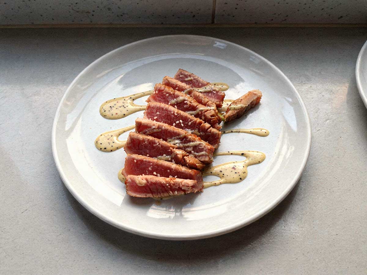 Een aan plakken gesneden tonijnsteak op een wit bord.