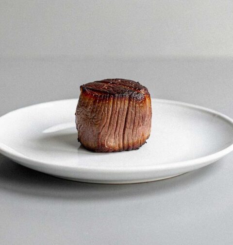Een kleine gebakken tournedos op een wit bord.