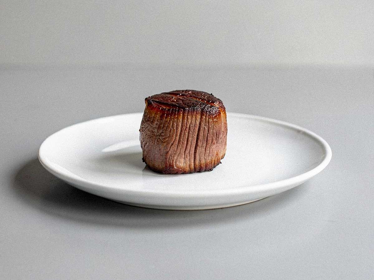 Een kleine gebakken tournedos op een wit bord.